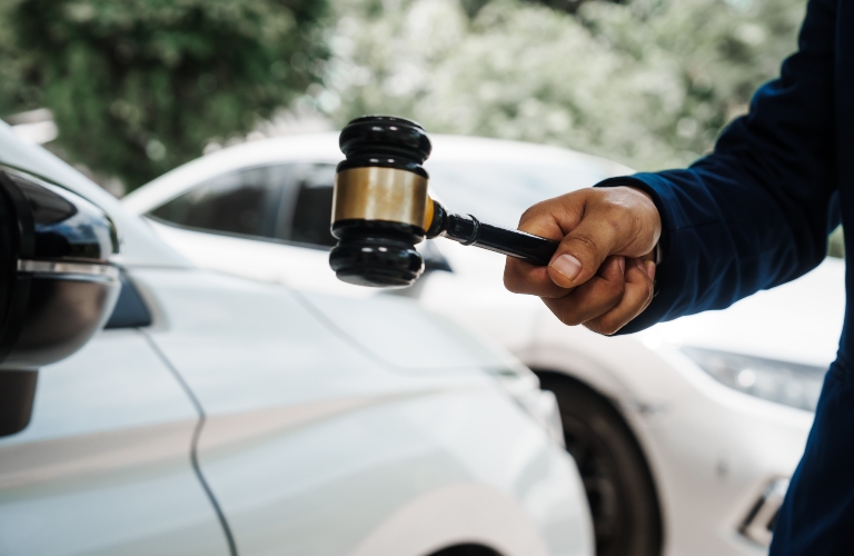 a lawyer holding a wooden gavel and standing in front of a car